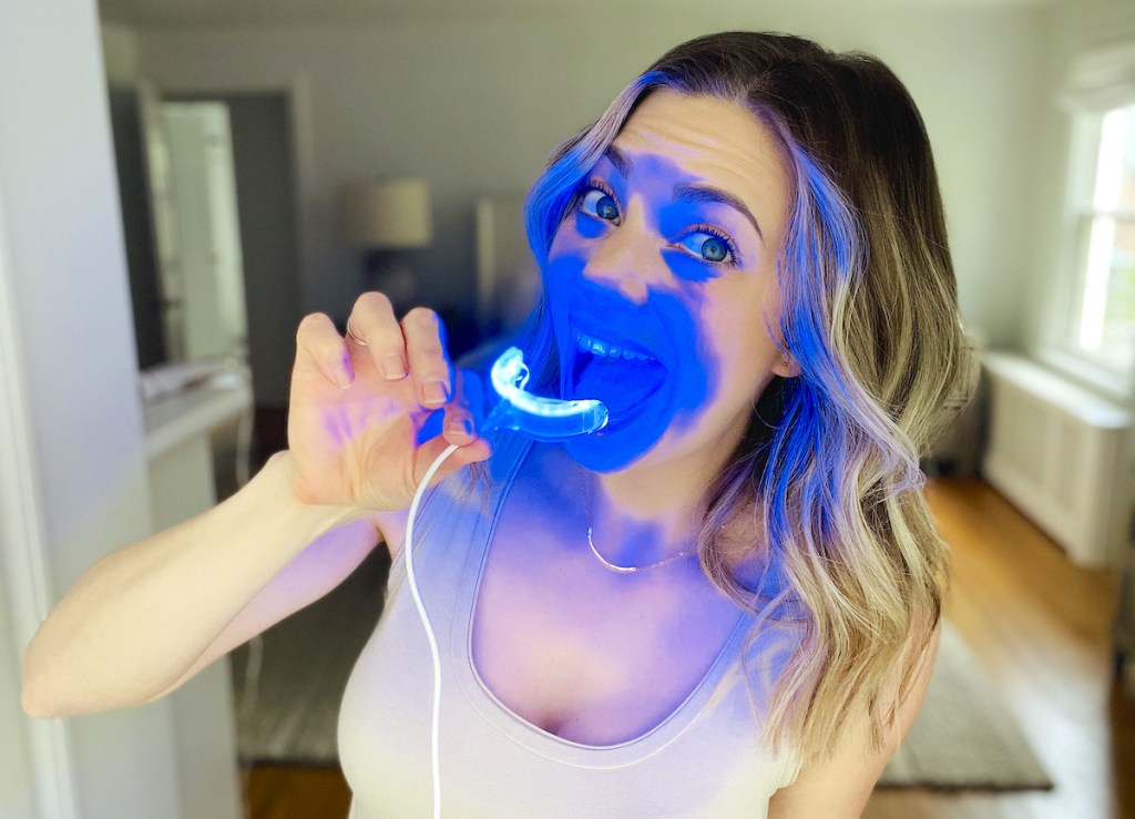woman holding blue snow teeth whitening tray in front of face with blue led light on