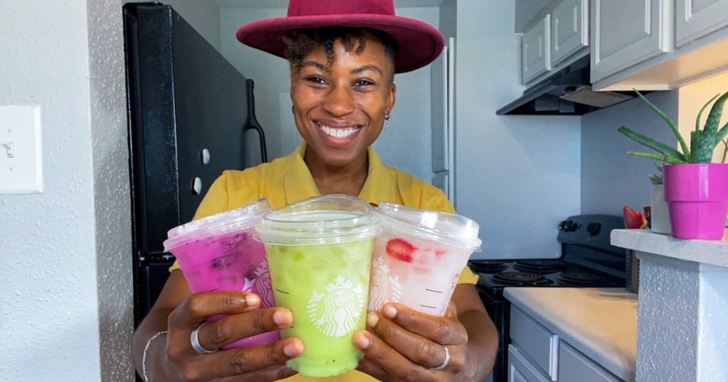 woman in hat holding 3 iced Starbucks drinks