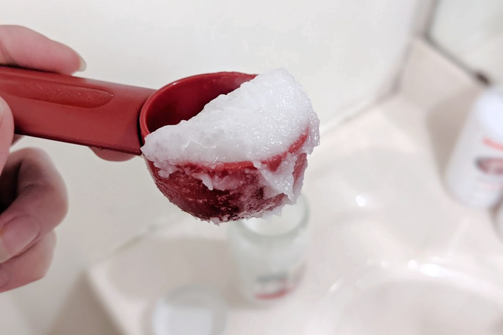 coconut oil in a tablespoon measurer with jar in background