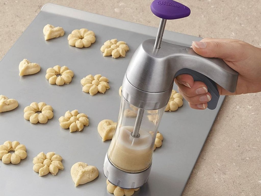 hand using cookie press on baking sheet