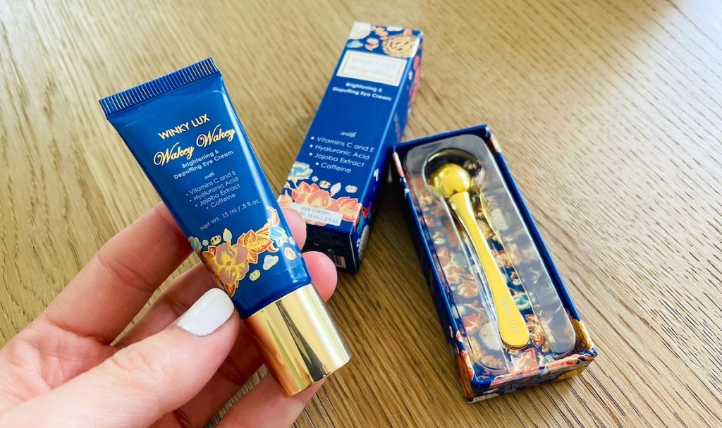 hand holding tube of winky lux eye cream and packaging laying on table