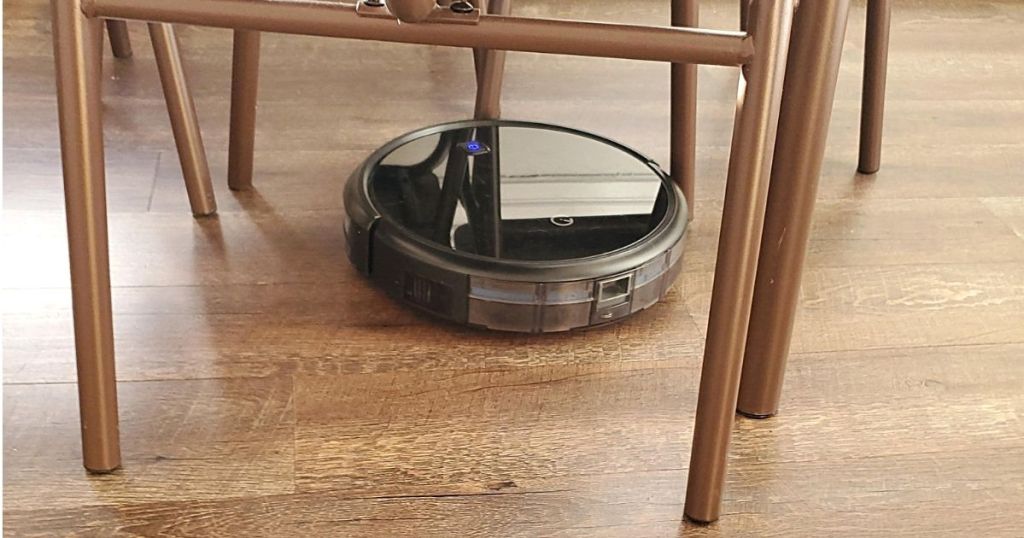 black robot vacuum under table cleaning wood floor