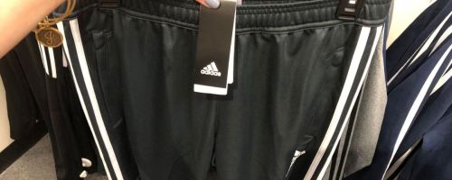 woman holding up hanger with men's Adidas shorts on it