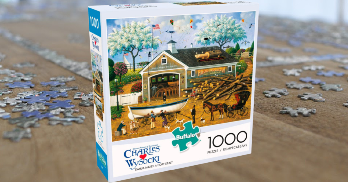 box containing a jigsaw puzzle featurine a barn and horses, on a table in front of a partially assembled puzzle