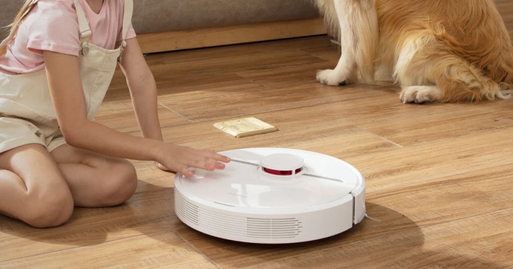white robot vacuum on wood floor near girl and dog
