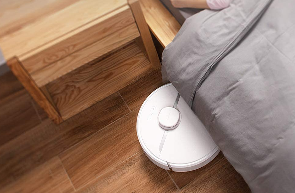 white robot vacuum cleaning under a bed