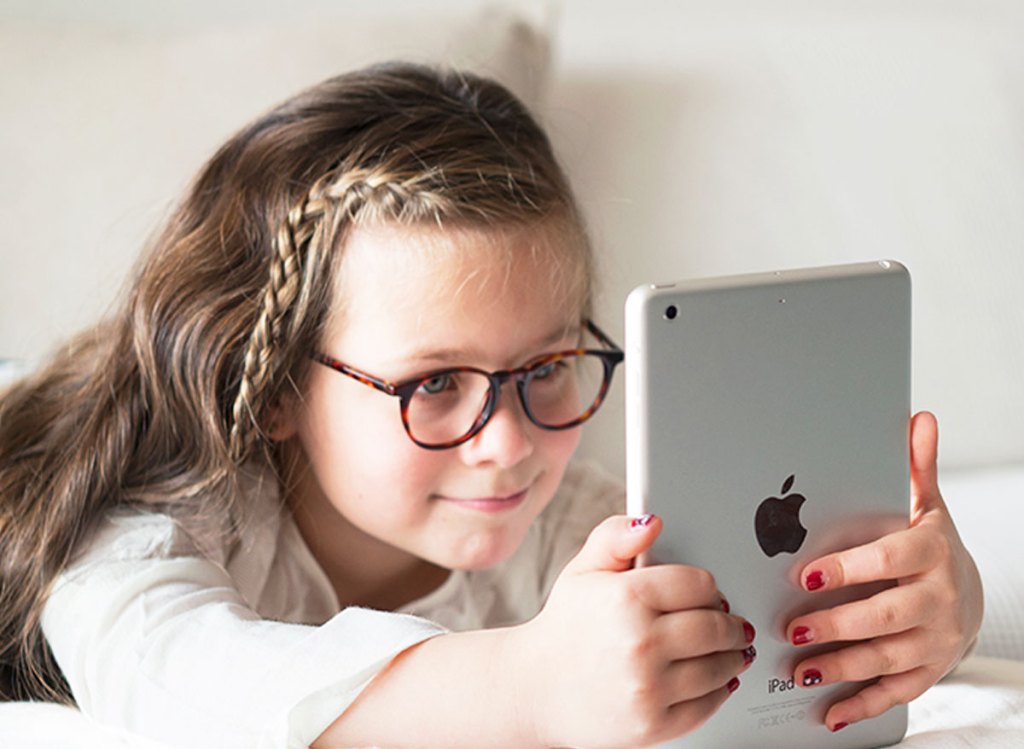 girl laying in bed holding ipad and wearing glasses