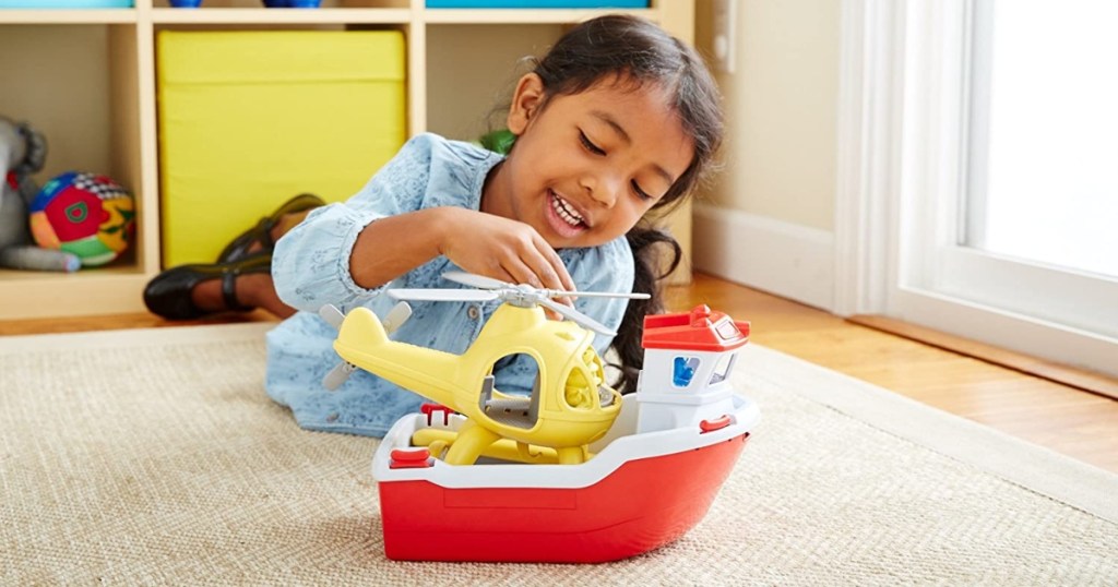 Green toys rescue boat on the floor with a little girl playing with the helicopter on top of the boat