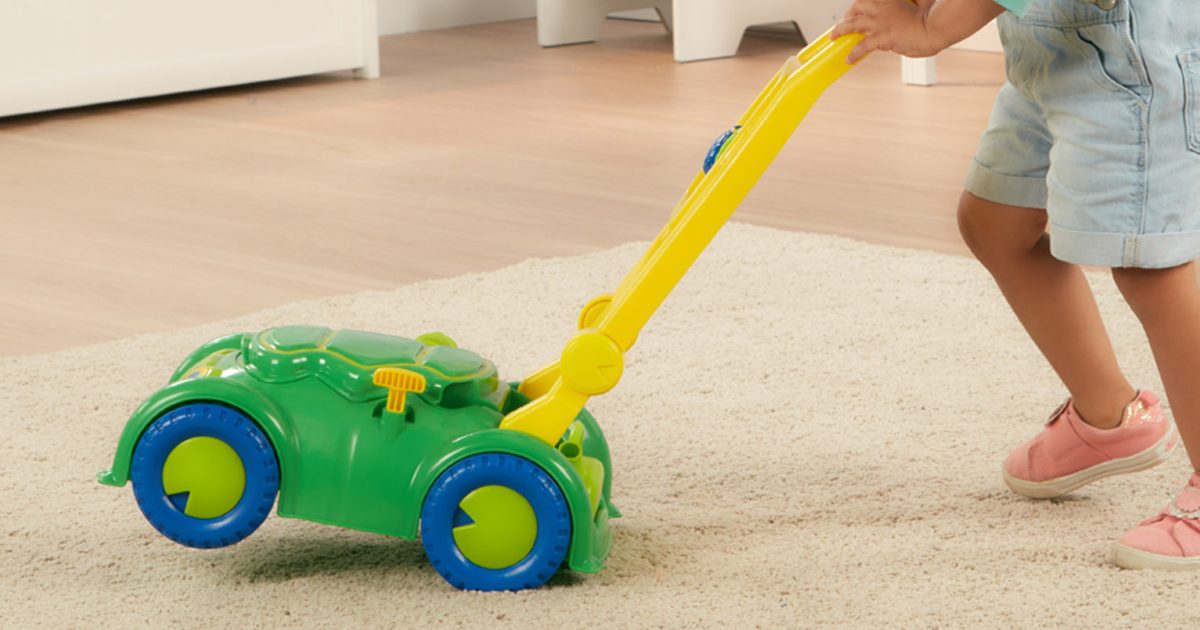 girl using toy lawn mower in living room