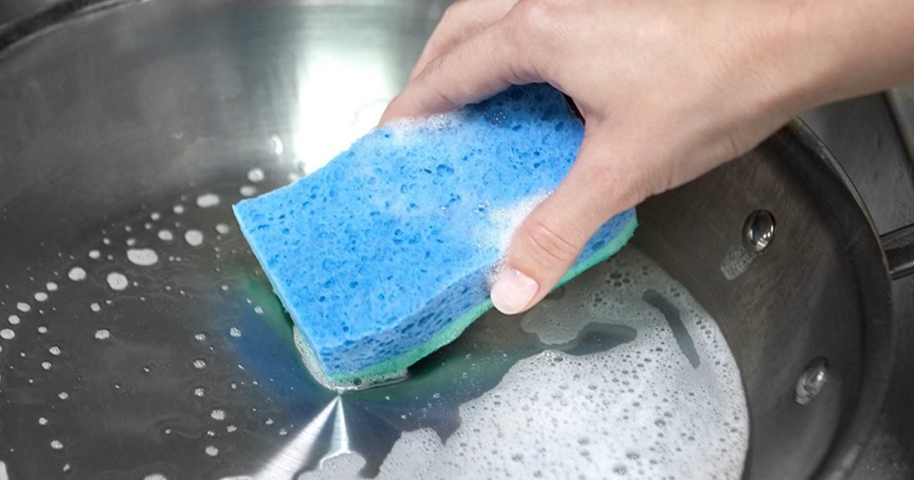 woman's hand cleaning pan with blue sponge