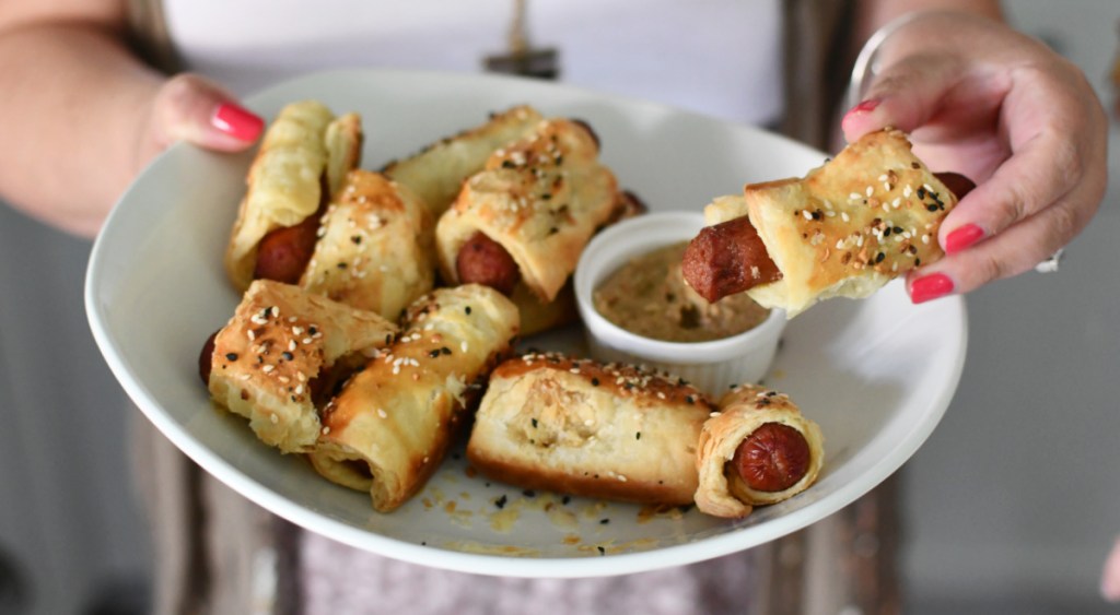 Woman holding a platter of pigs in a blanket puff pastry snacks