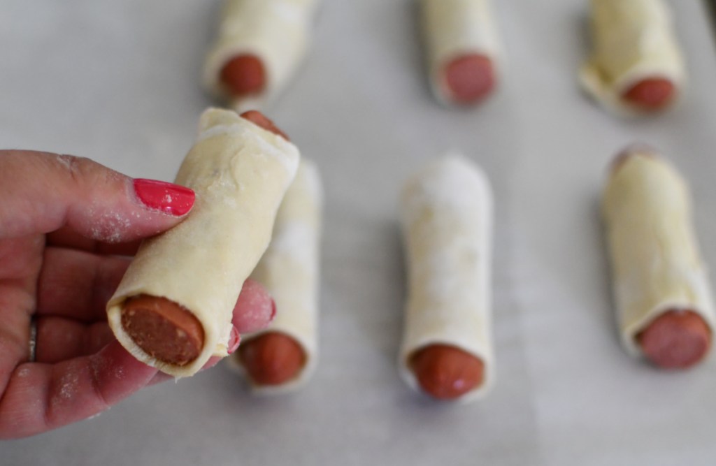 rolling hot dogs in puff pastry dough to make pigs in a blanket