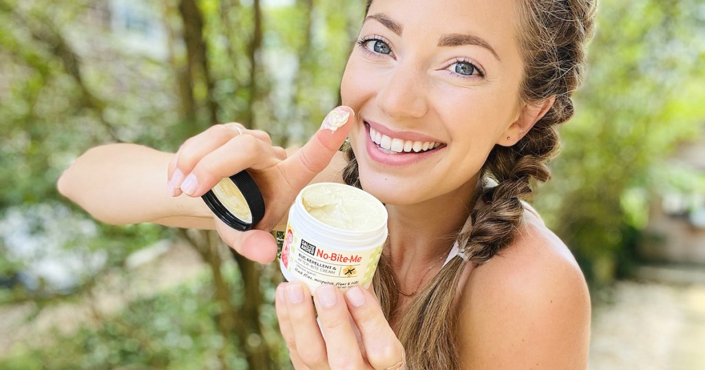 woman holding container of natural bug repellent cream smiling outside