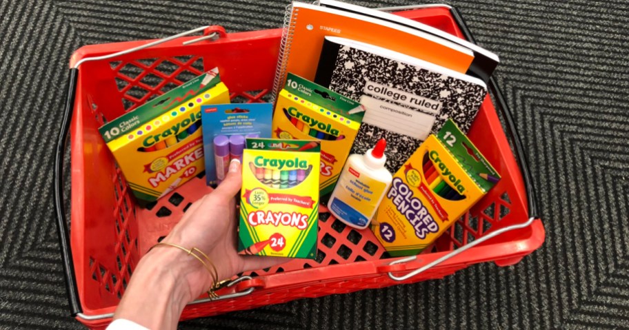 holding box of crayons near Staples basket full of school supplies