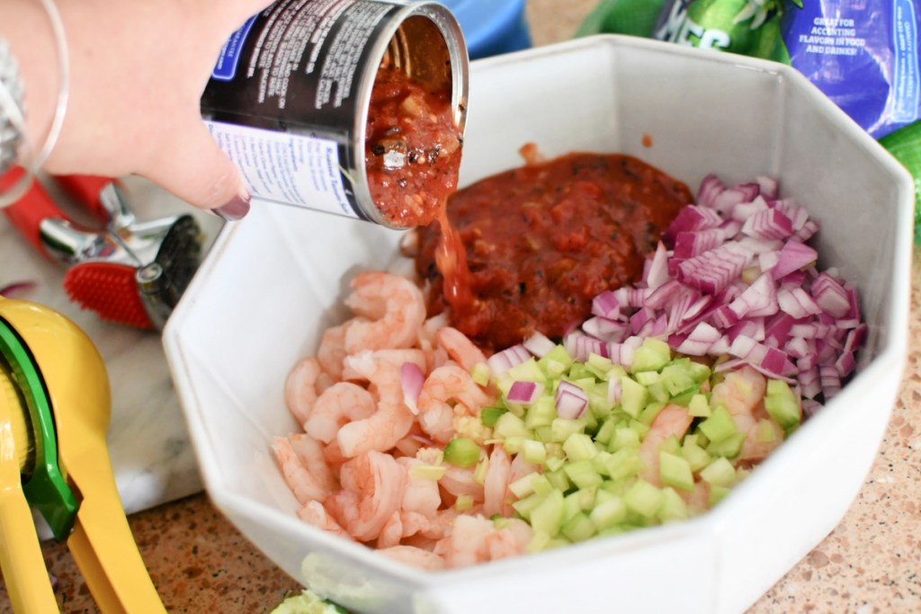 adding diced tomato to mexican shrimp cocktail bowl