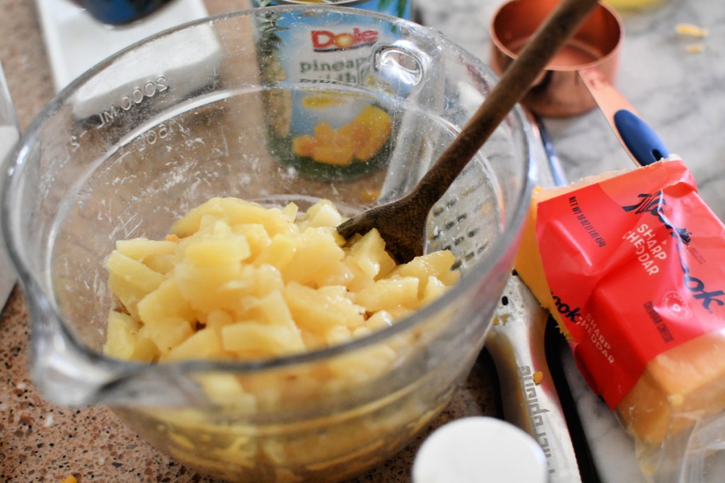 adding pineapple to mixing bowl with cheese