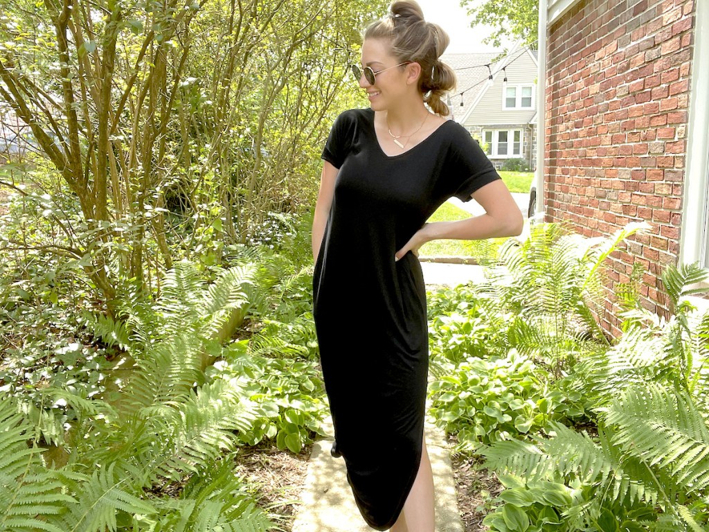 woman wearing black maxi dress and sunglasses standing on walkway surrounded by greenery
