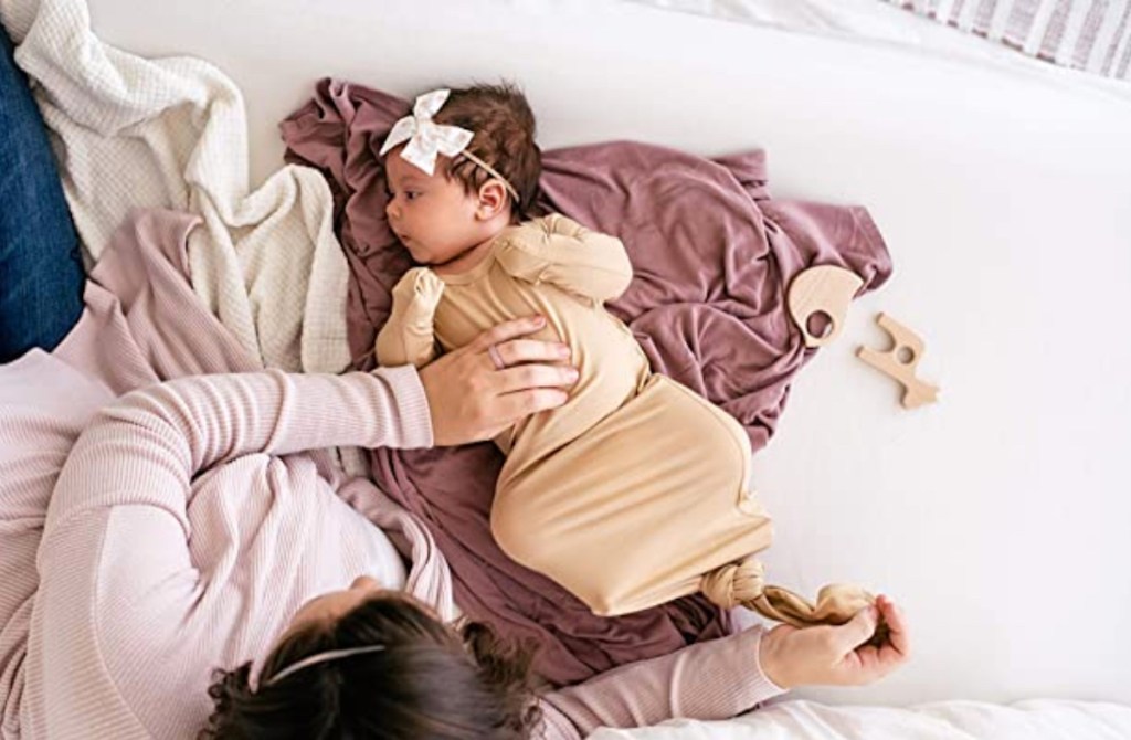 baby wearing nightgown and bow laying on bed with mom