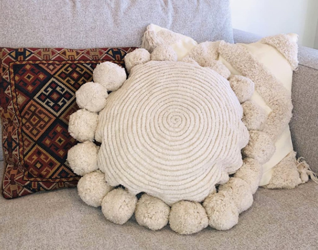 cream colored round throw pom pillow on couch 