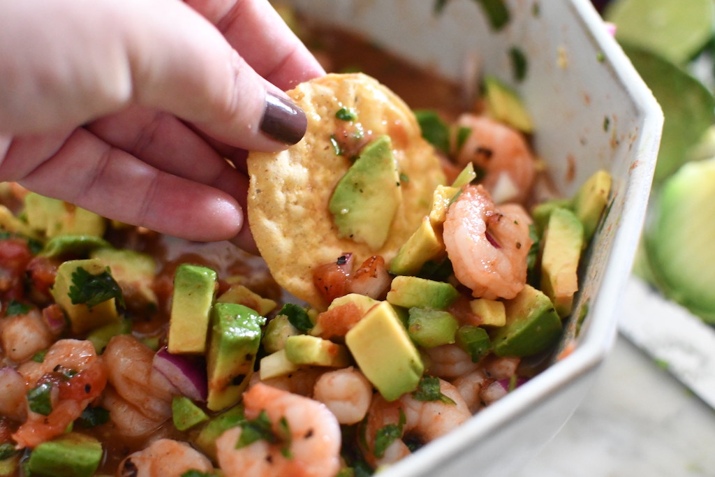 dipping tortilla chip in Mexican shrimp cocktail 
