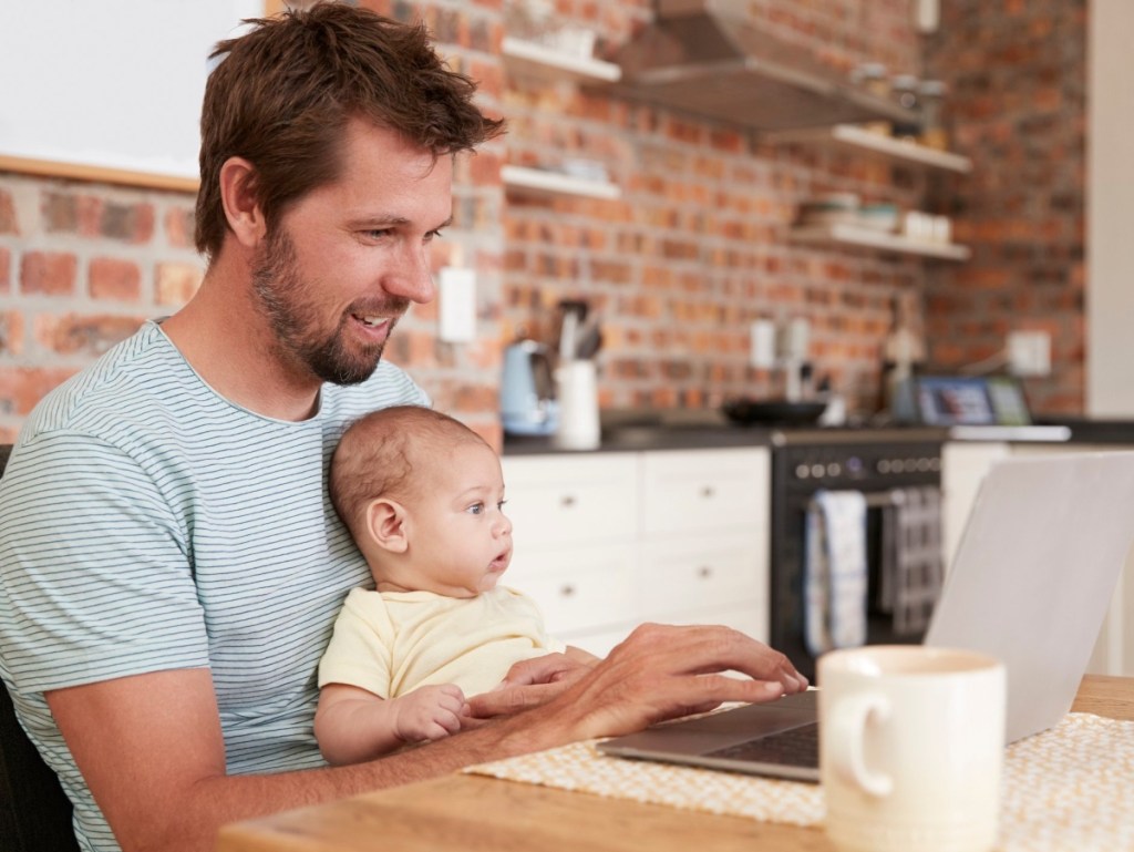 man using laptop while holding baby