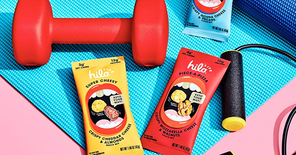 three different narrow bags of Hilo snacks on a yoga mat with workout equipment 