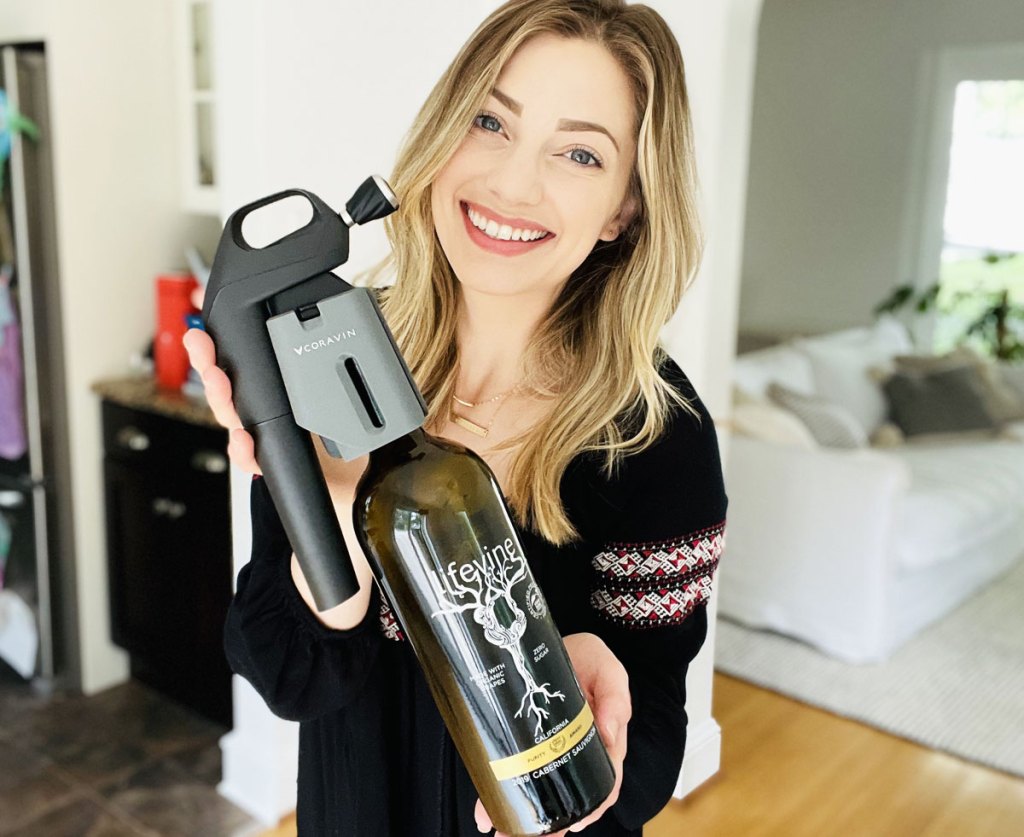 woman with blonde hair holding up bottle of wine with preservation system on it