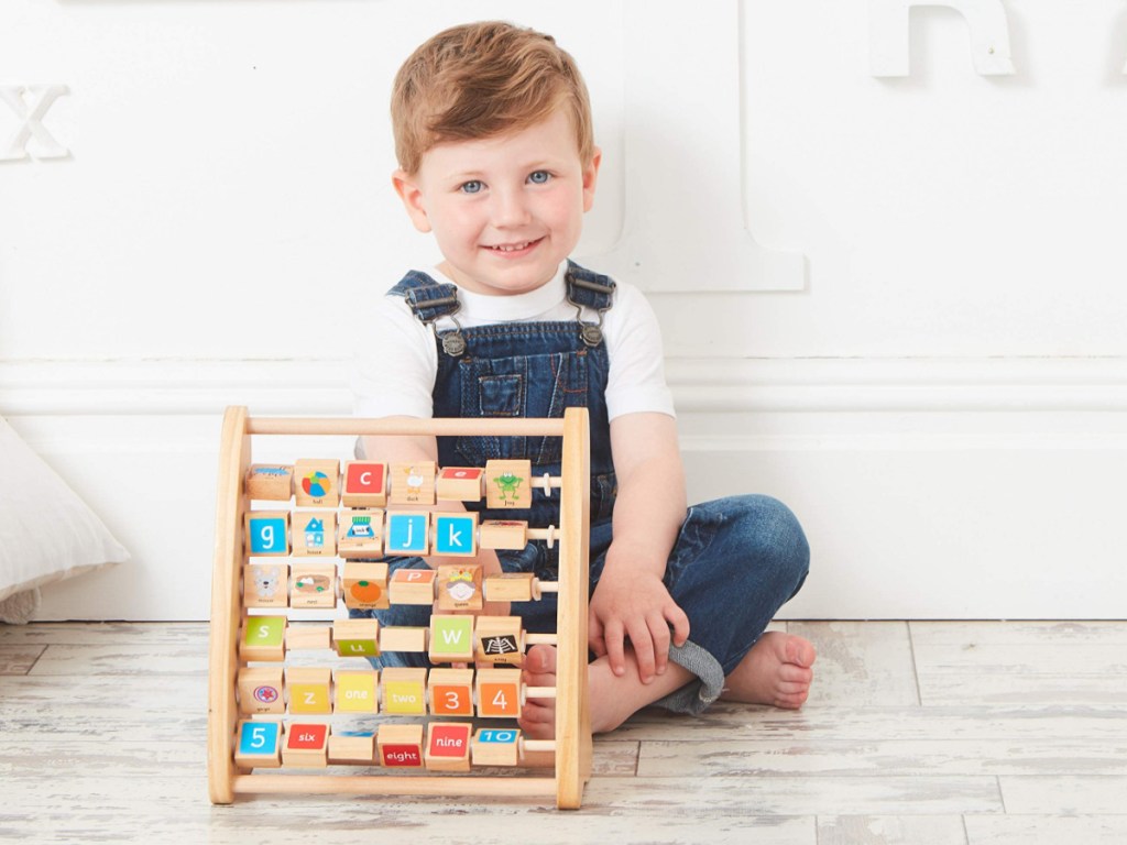 little boy sitting on the floor with a wooden alphabet frame