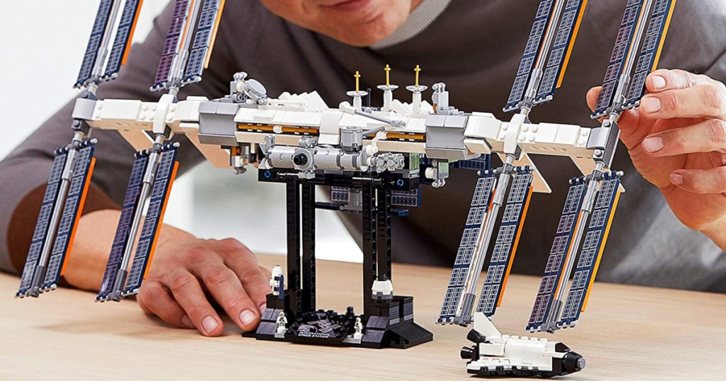 man sitting behind a LEGO space station admiring the construction