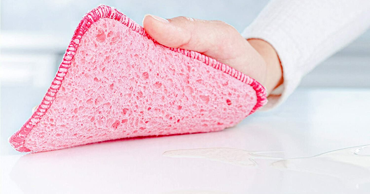hand using a pink scrub pad on a counter with the corner lifted up to show the bottom