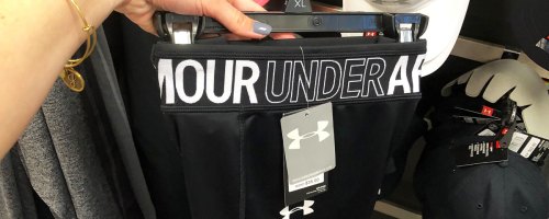 woman holding up black pair of under armour shorts on hanger
