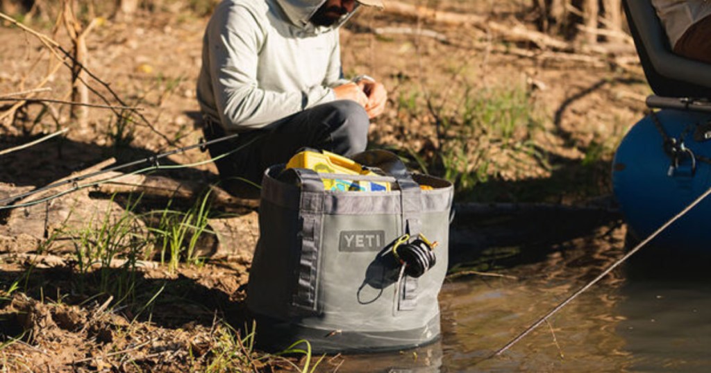 man squatting next to water with a yeti carryall