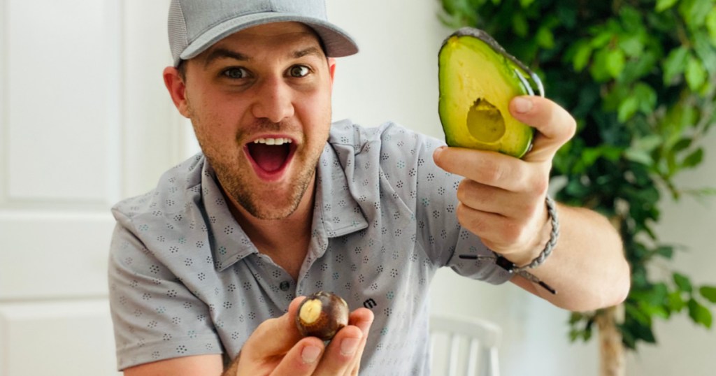 man holding half of an opened avocado with pit taken out