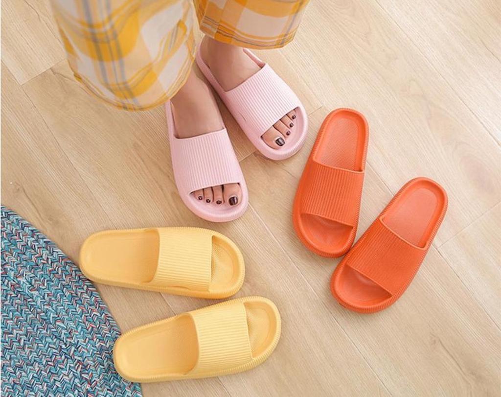 feet wearing pink house shoes with yellow and orange pair laying on wood floor