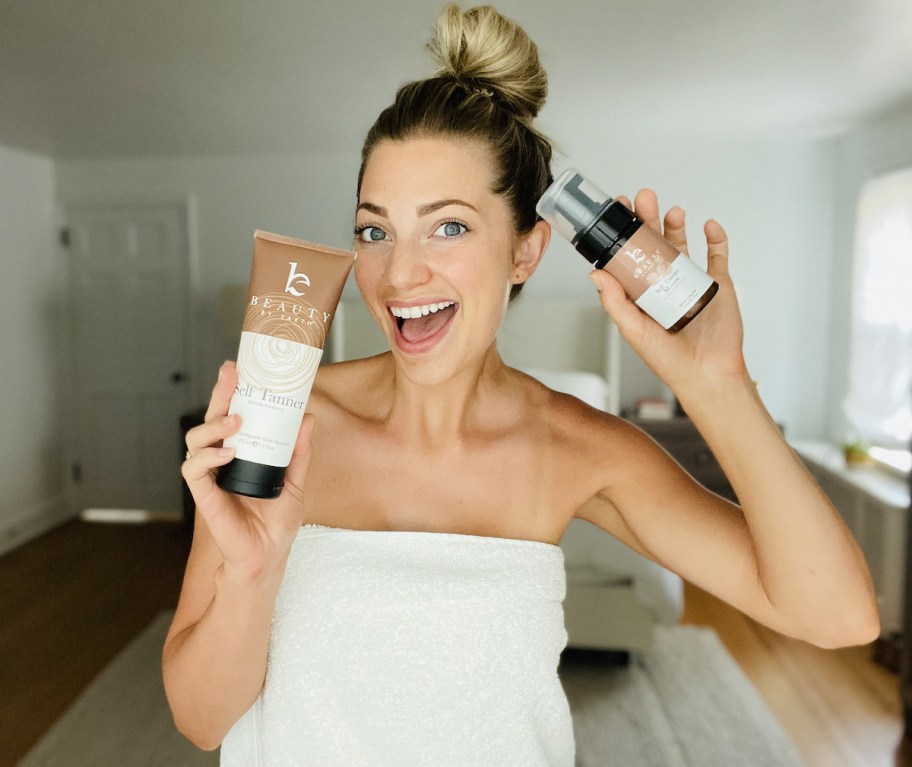 woman wearing white towel holding up beauty products