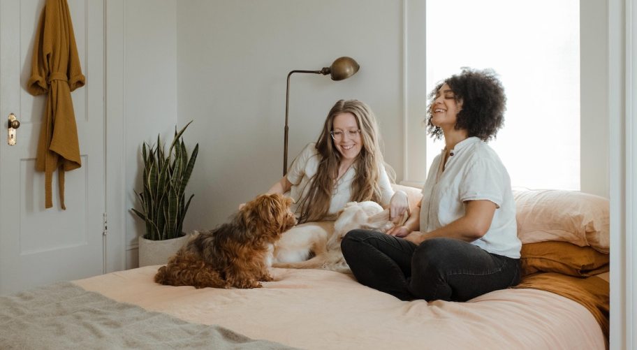 two women with dogs sitting on bed laughing