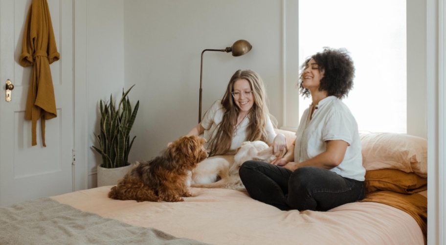 two women with dogs sitting on bed laughing