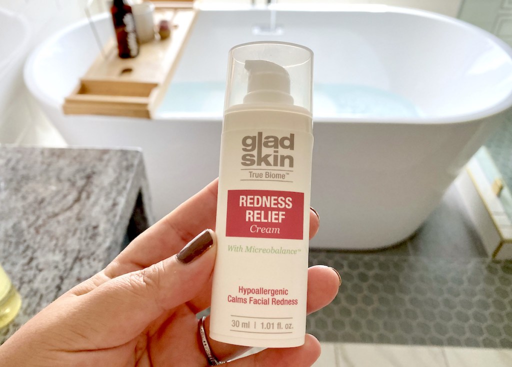 hand holding a bottle of gladskin skincare for redness relief cream in front of bathtub