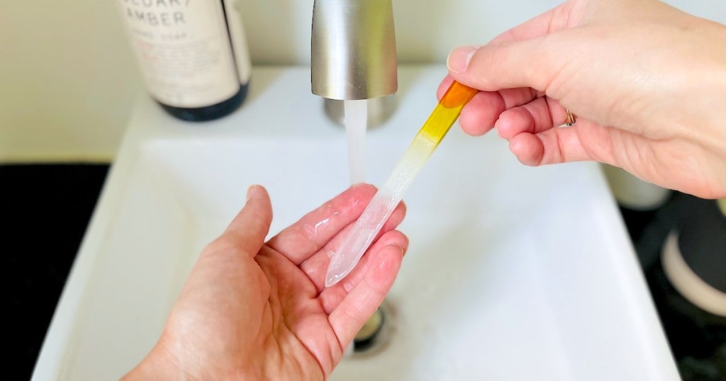 hands holding glass nail file under running water in sink