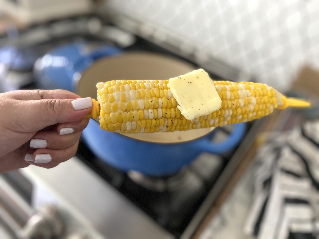 holding boiled corn on the cob with butter