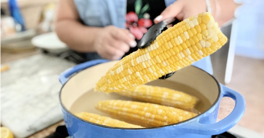 holding up corn on the cob over a pot 