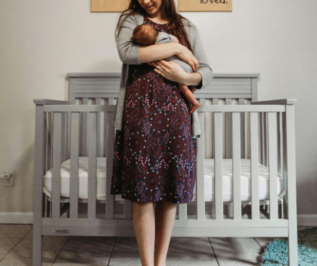 woman holding baby in front of nursery crib