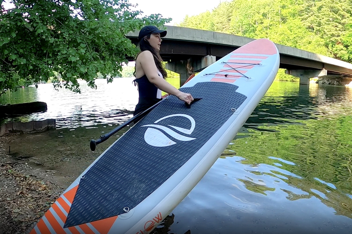 Woman holding an inflatable paddle board walking into the water