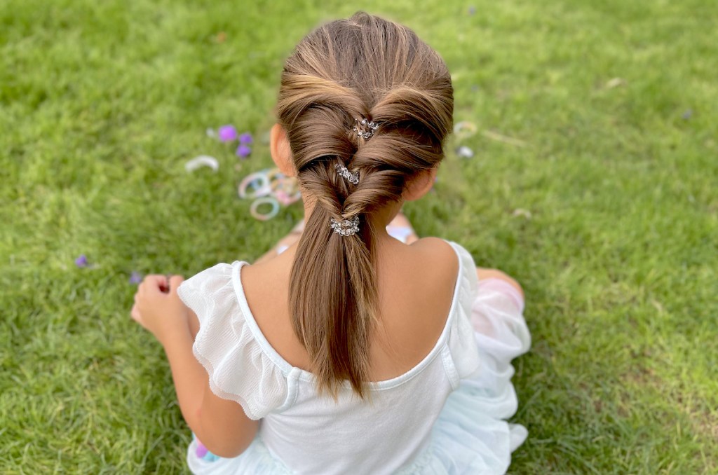 girl sitting in grass with styled hair wearing clear teleties coiled hair ties