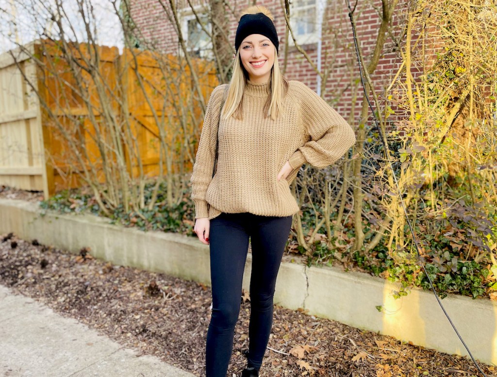 woman wearing sweater leggings and hat standing outside on sidewalk