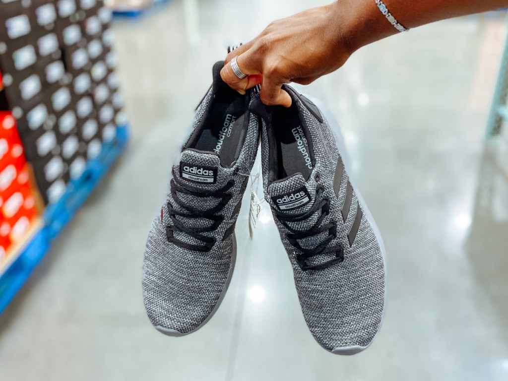 Woman holding gray mesh pair of Adidas Mens Shoes at Costco