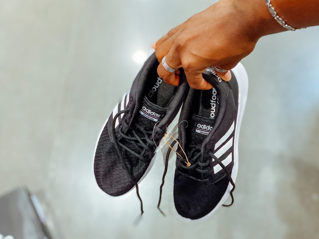woman holding pair of black Adidas QT Racer Shoes