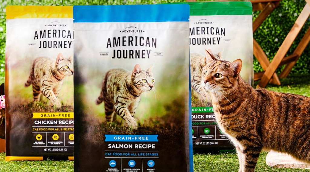 cat standing next to three bags of cat food