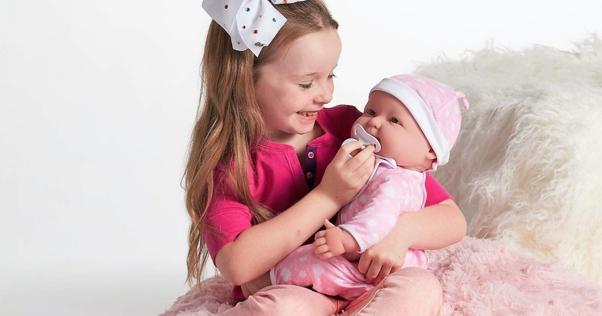 girl sitting on a fuzzy chair holding a baby doll wearing a pink hat and outfit