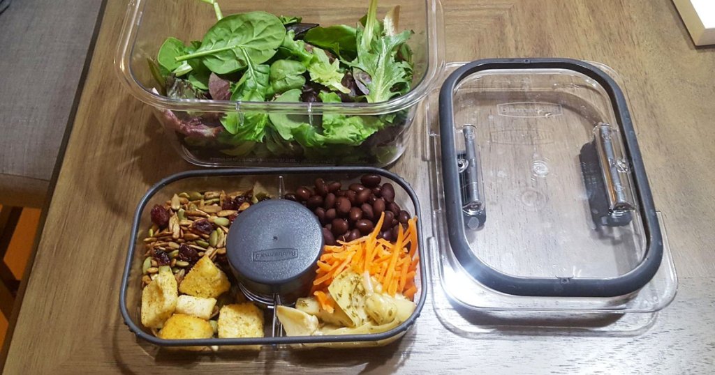 salad greens and toppings in lunch storage container on wood table